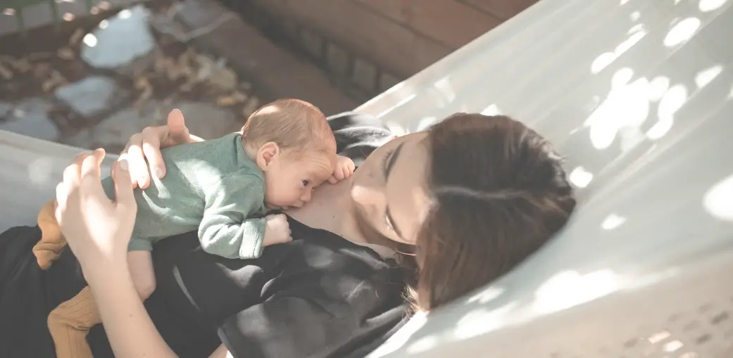Madre amamantando a su bebé en una hamaca, reflejando la intimidad de la lactancia en medio de la presión social y viviendo una maternidad juzgada.
