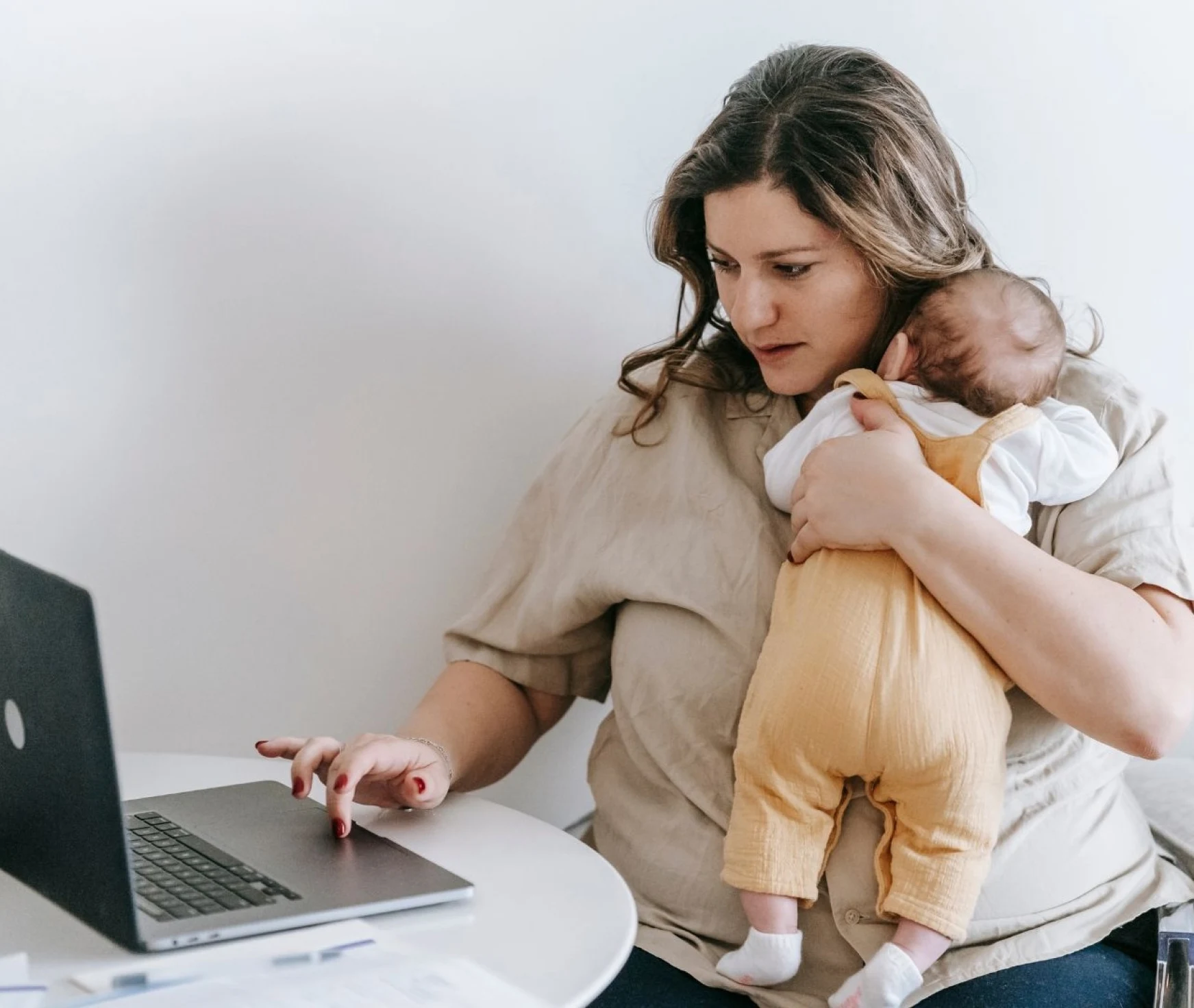 Una madre sujetando a su bebé mientras trabaja en su portátil, simboliza una madre que ha perdido en el camino y no sabes quién es después de ser madre. Que la soledad y el aislamiento emocional son constantes. Que la presión por ser una madre perfecta le está pasando factura. Que el estrés y el desbordamiento emocional son parte de su día a día. Que sus expectativas sobre la maternidad no se están cumpliendo. Rocío Mesa. Terapéuta emocional y life coach para madres. Presencial y online en Palma de Mallorca